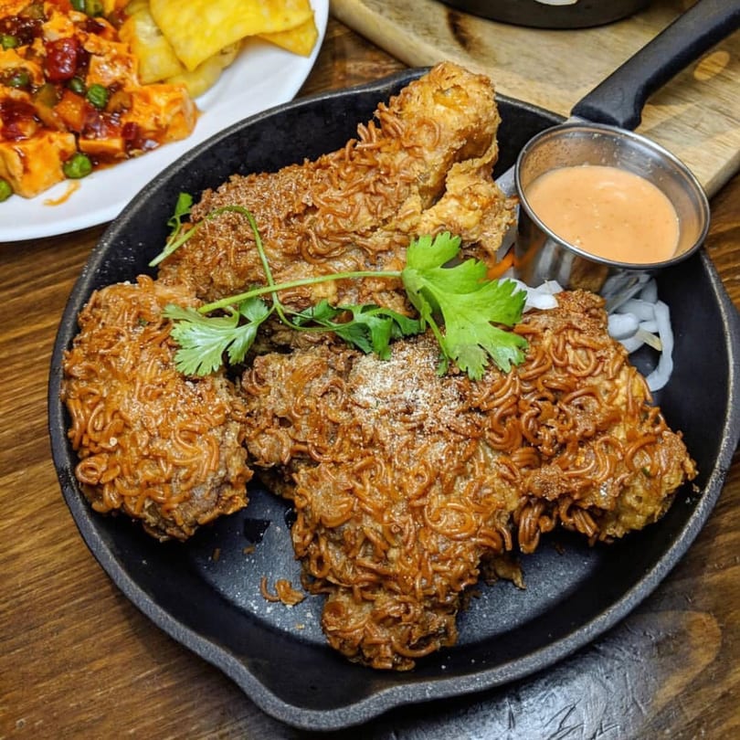 Double Chin's ramen-crusted fried chicken in a skillet with dipping sauce and cilantro garnish.