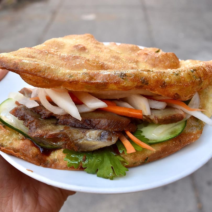 A Double Chin scallion pancake sandwich filled with duck, pickled vegetables, and cilantro, held on a white plate.